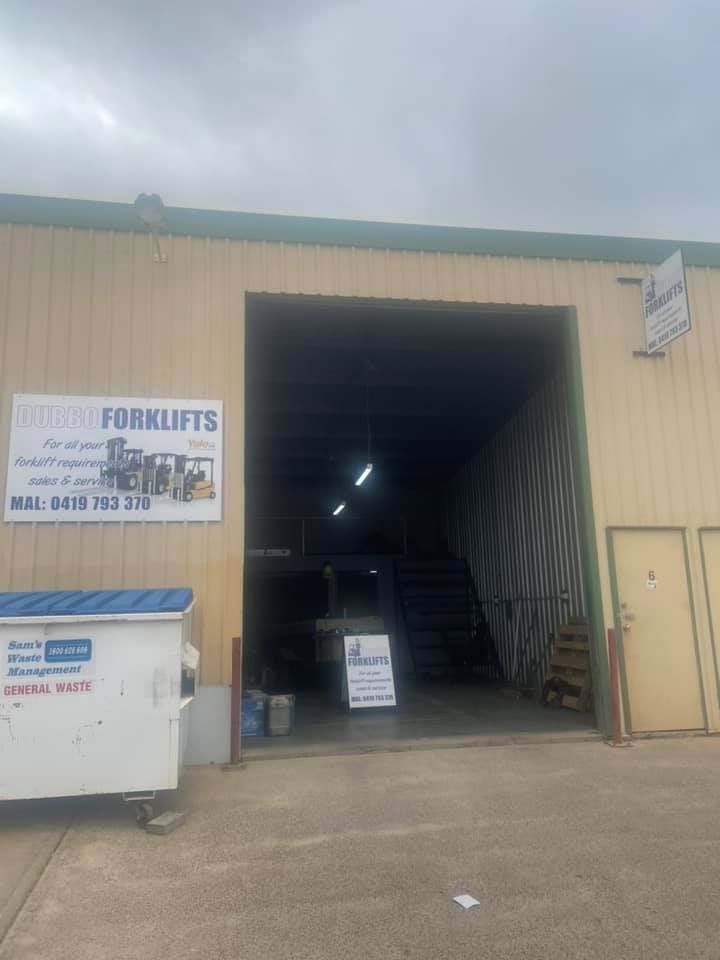 Building entrance with a forklift business sign, a dumpster, and an open doorway.