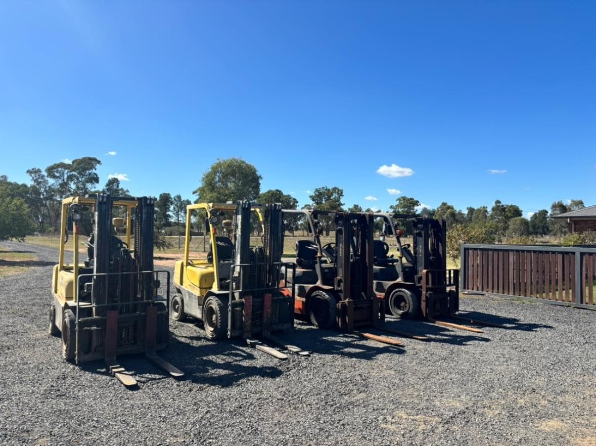 Five forklifts parked in a gravel lot under a bright blue sky.