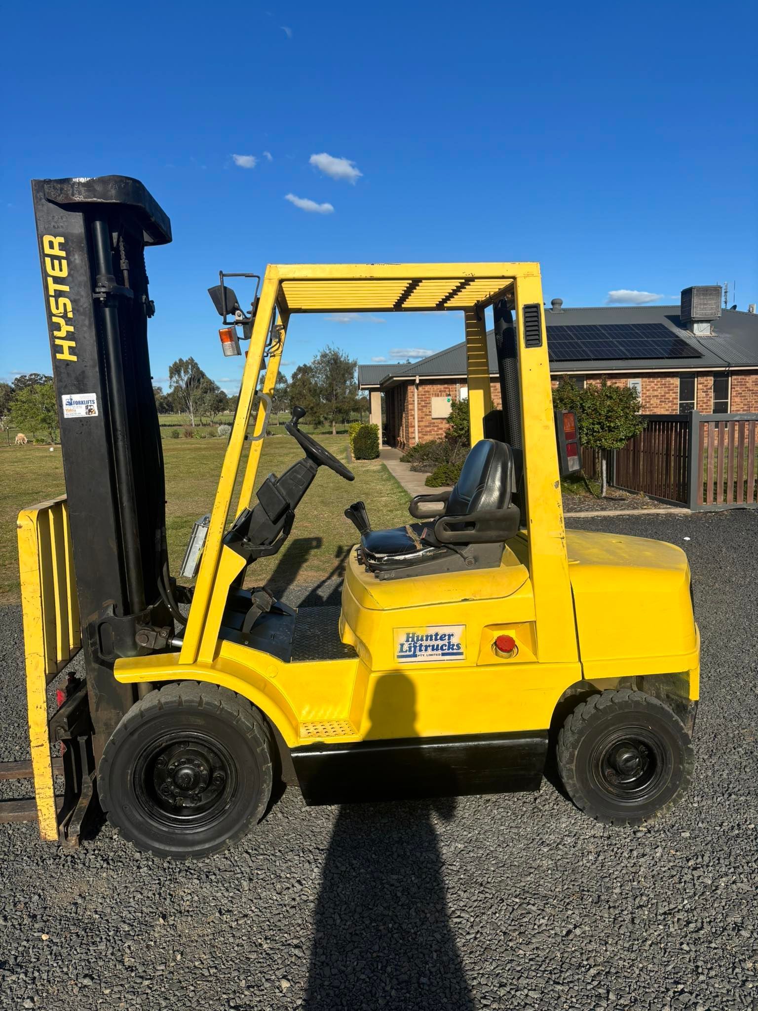 Yellow Hyster forklift parked on gravel with a residential background, under a blue sky.