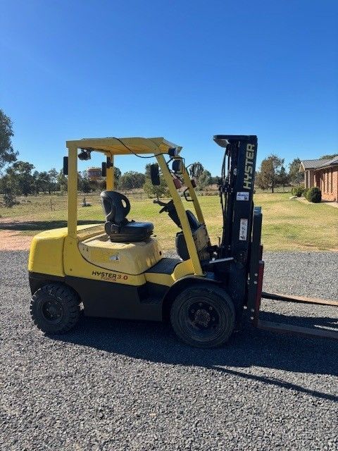 Yellow Hyster forklift parked on gravel, in a rural setting under a blue sky.