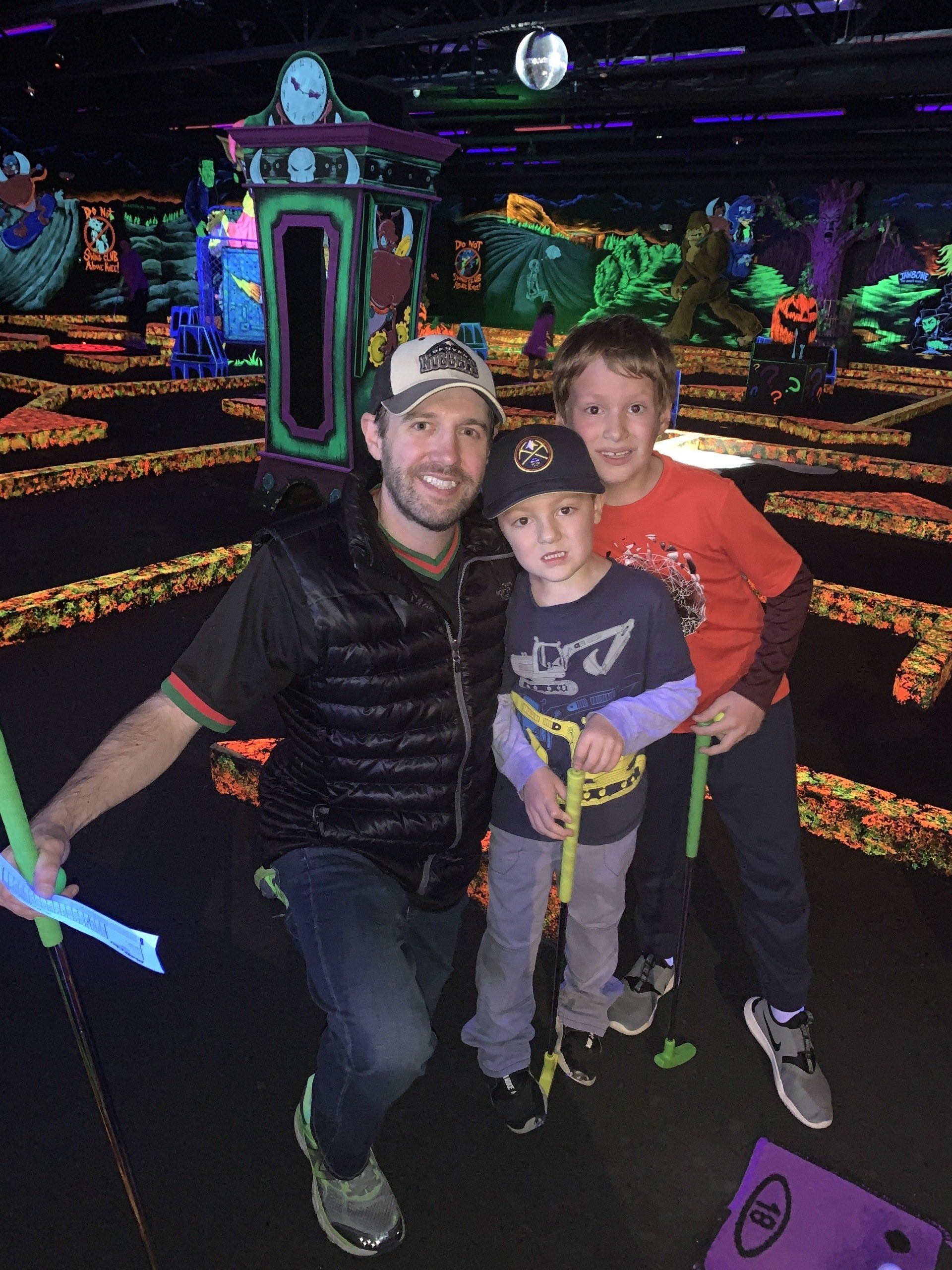 A man and two young boys are posing for a picture at a mini golf course