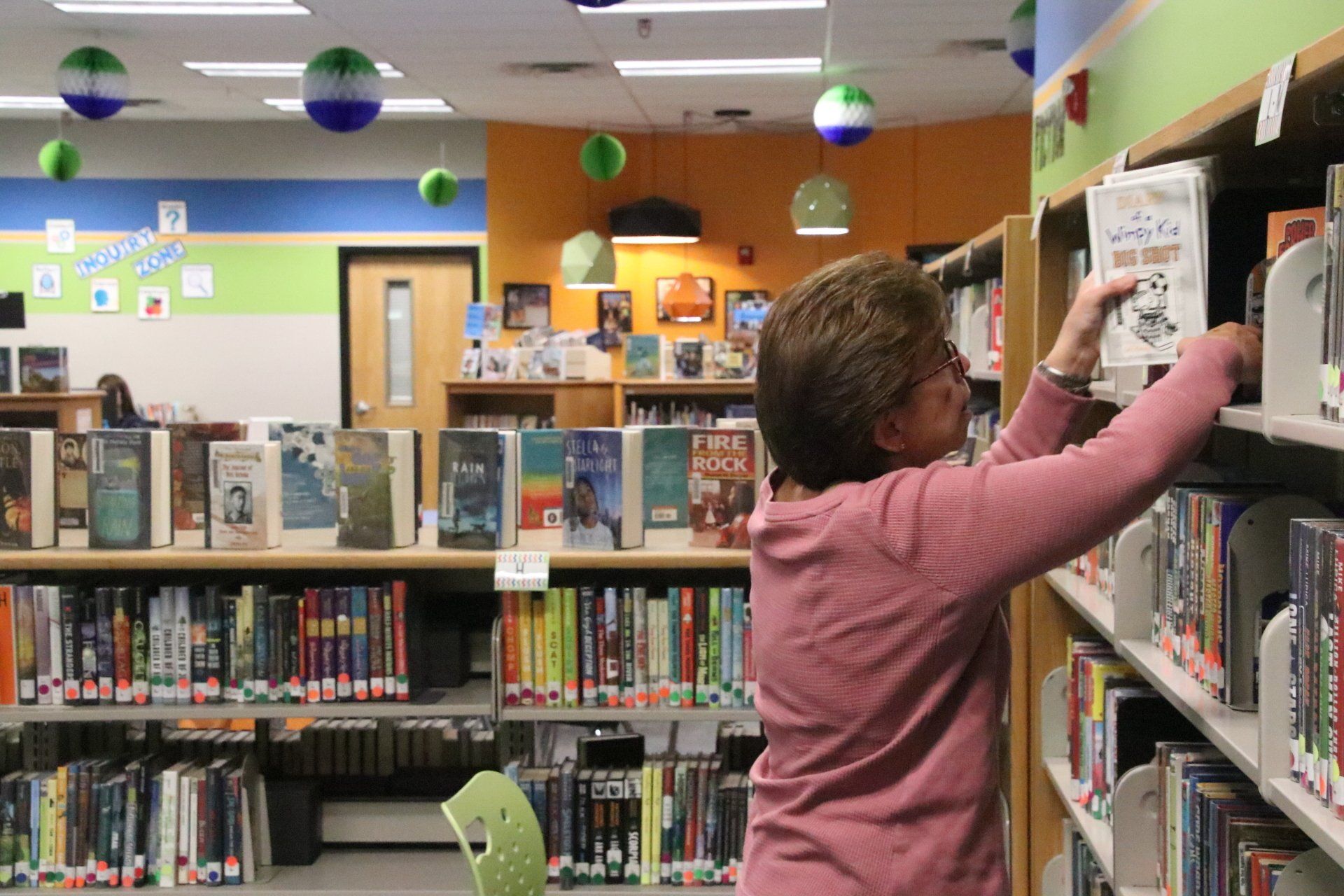 A woman is reaching for a book in a library