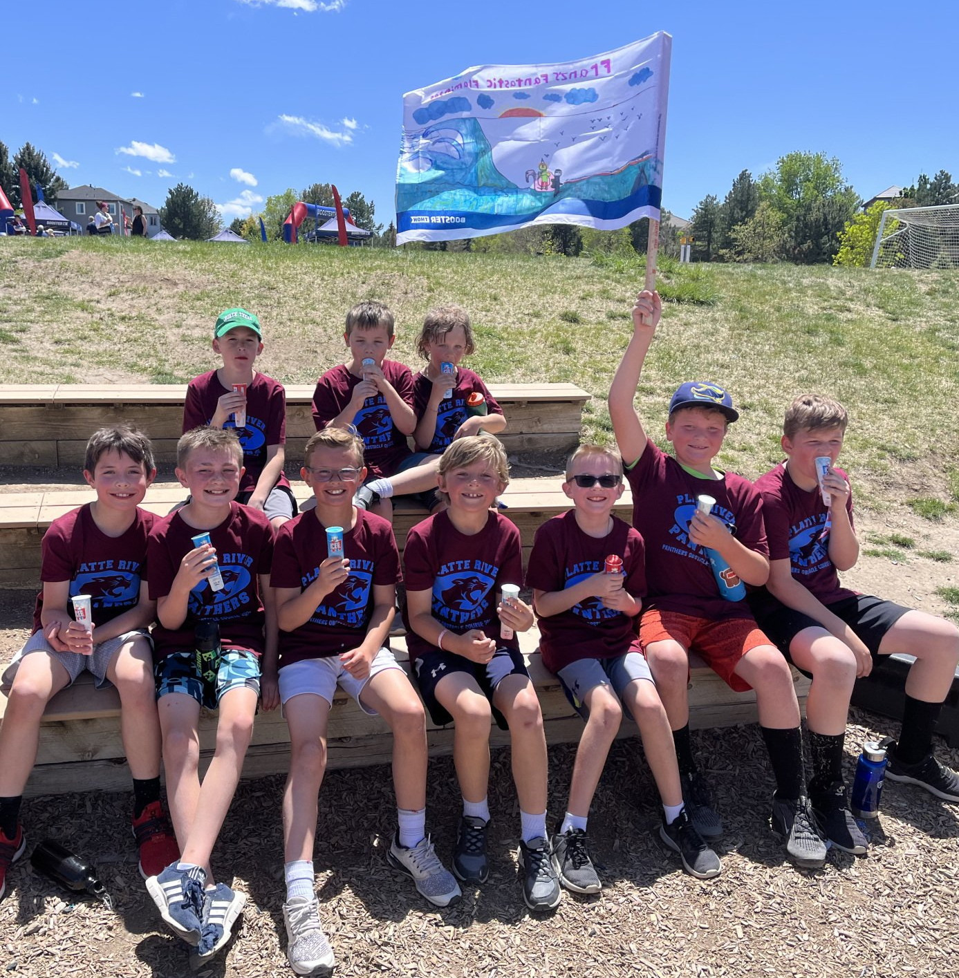 A group of young boys are sitting on a bench holding ice cream and a flag.