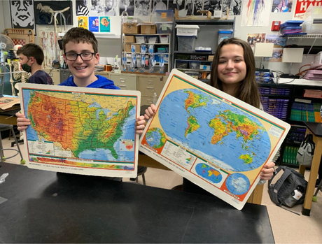 A boy and a girl are holding maps of the united states and the world.