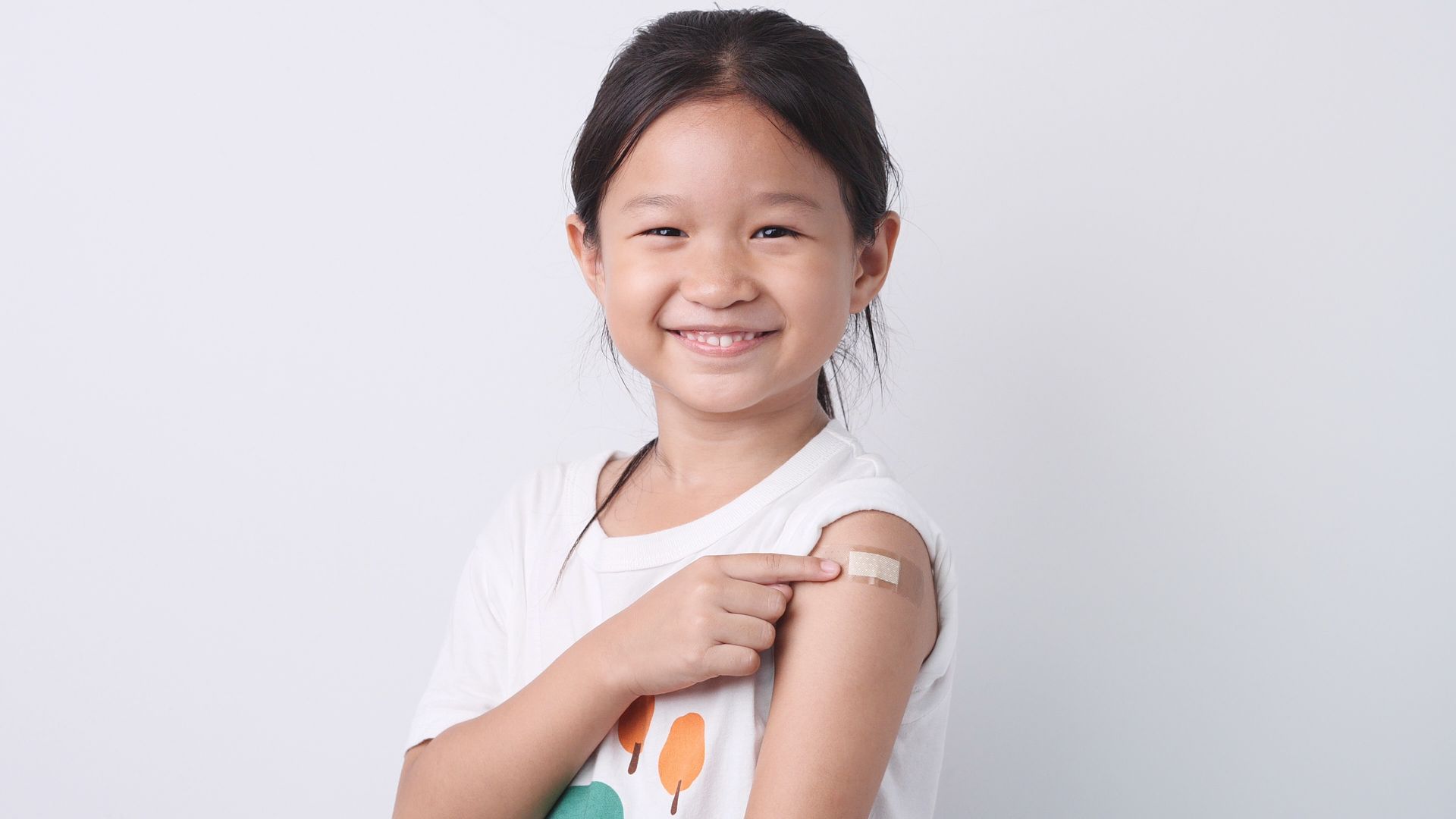 young girl of elementary school age smiling and holding sleeve up to show badage after receiving a vaccine
