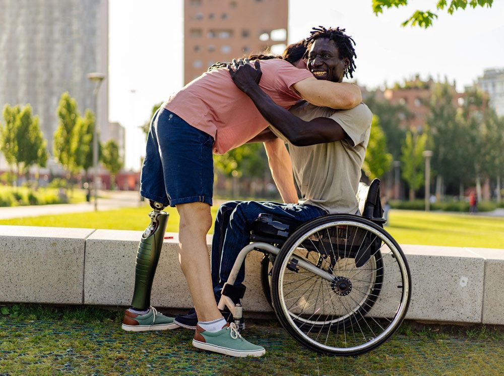 A Man with A Prosthetic Leg Is Hugging Another Man in A Wheelchair — Mobility Modification Services In Garbutt, QLD