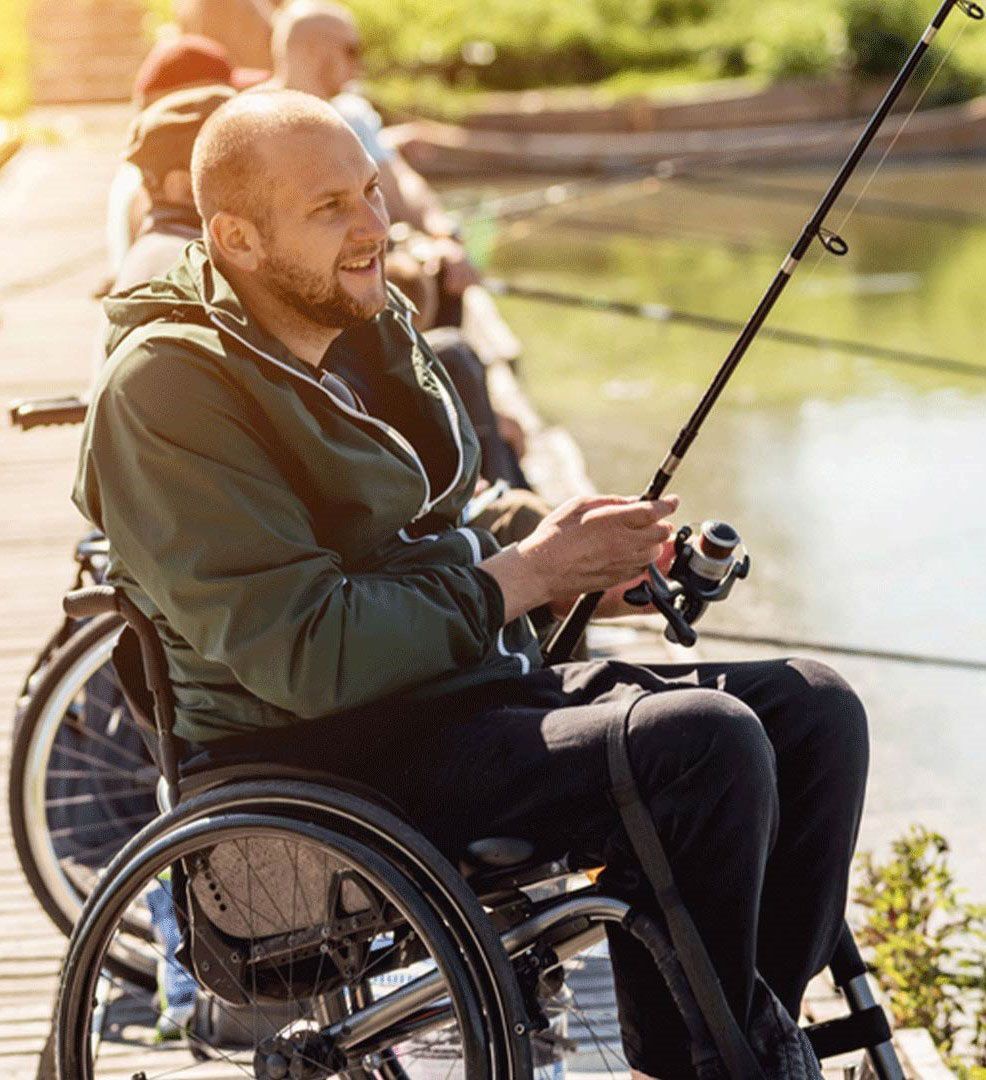A Man in A Wheelchair Is Fishing by The Water — Mobility Modification Services In Garbutt, QLD