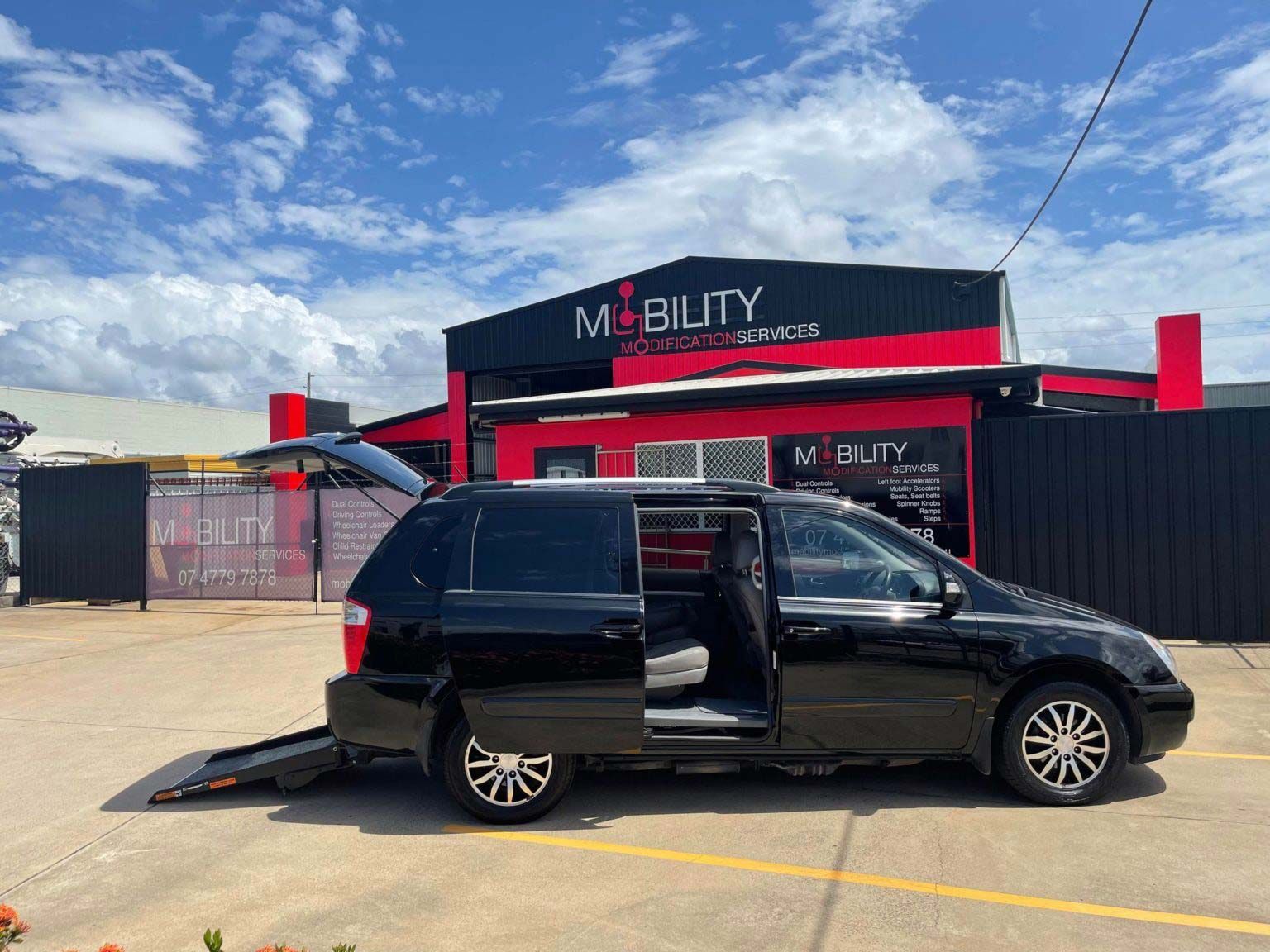 A Black Van with A Ramp Attached to It Is Parked in Front of A Building — Mobility Modification Services In Garbutt, QLD