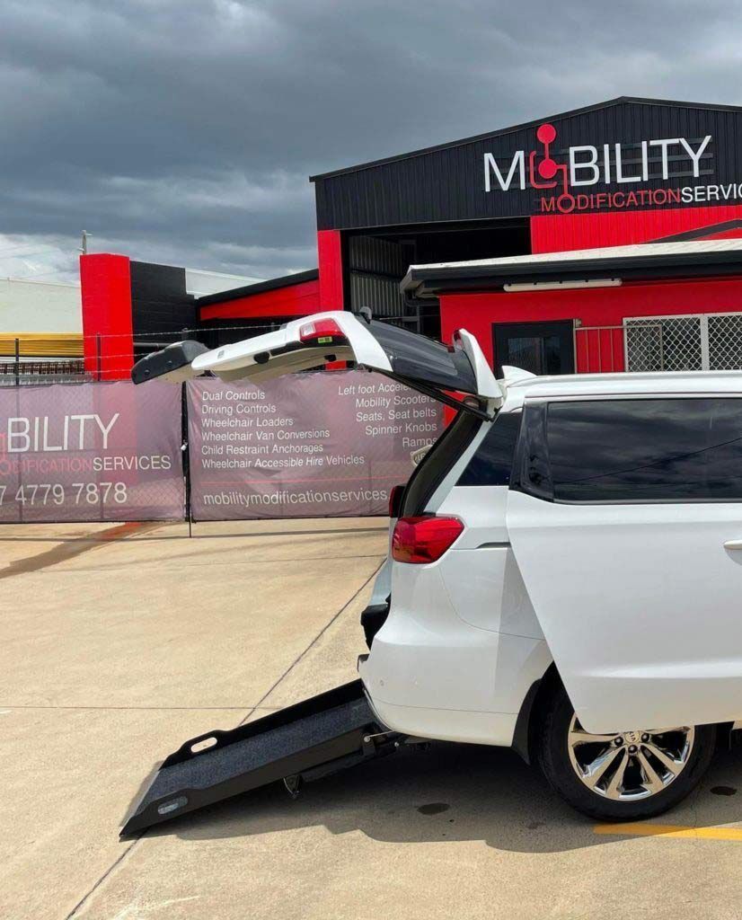 A White Van with A Wheelchair Ramp Is Parked in Front of A Building — Mobility Modification Services In Garbutt, QLD