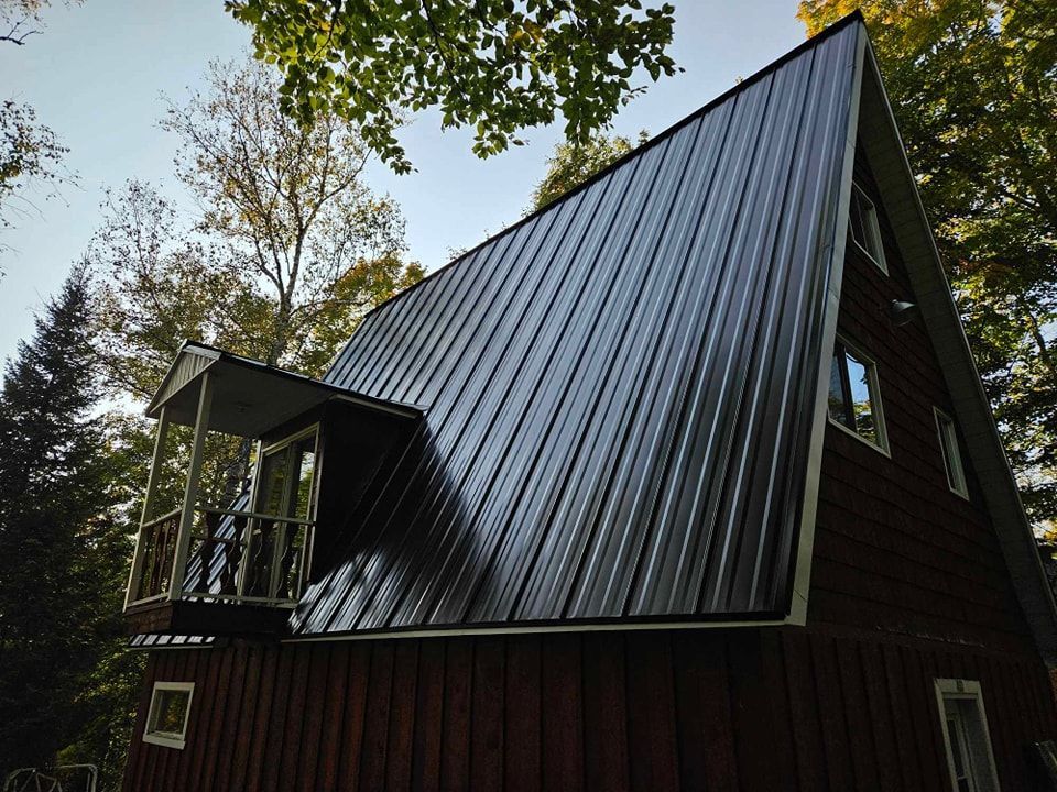 Une maison rouge avec un toit en métal noir et un balcon.