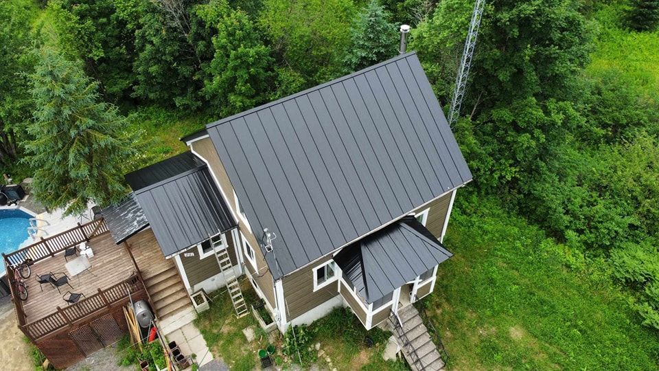 Une vue aérienne d'une maison au toit noir au milieu d'une forêt.