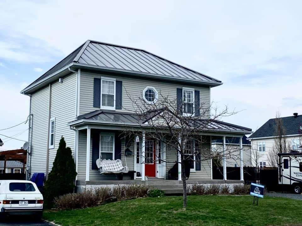 Une maison blanche avec un toit en métal et des volets noirs