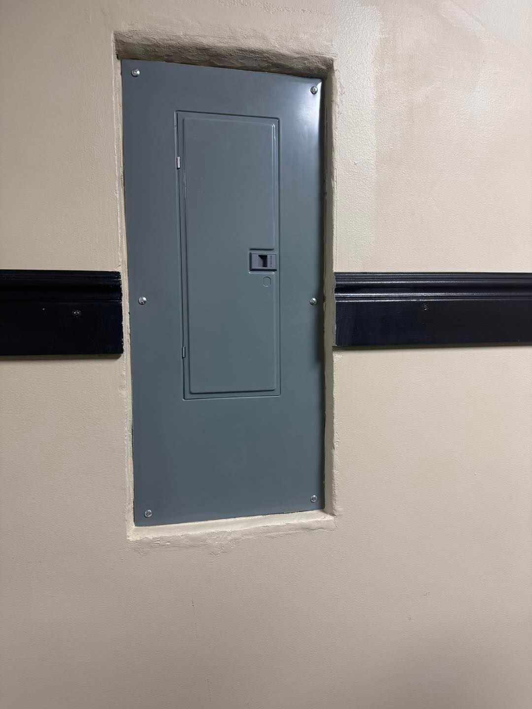 Electrical panel recessed in a light tan wall, surrounded by a light-colored frame.