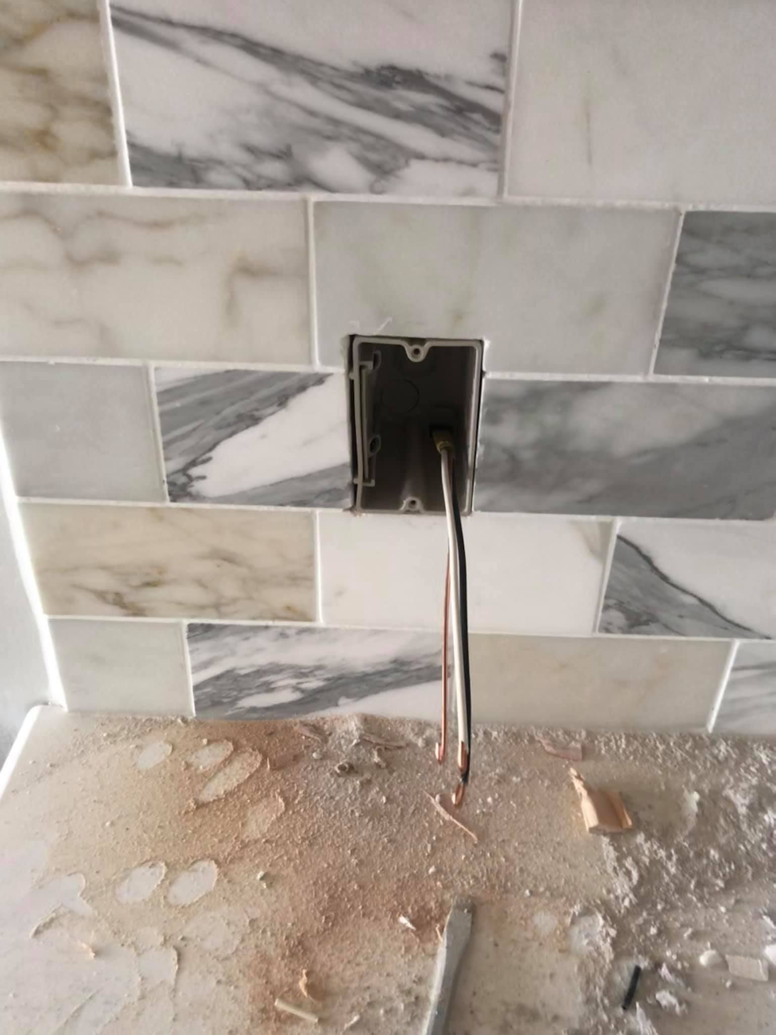 Marble backsplash with electrical outlet, wires exposed, construction debris below.