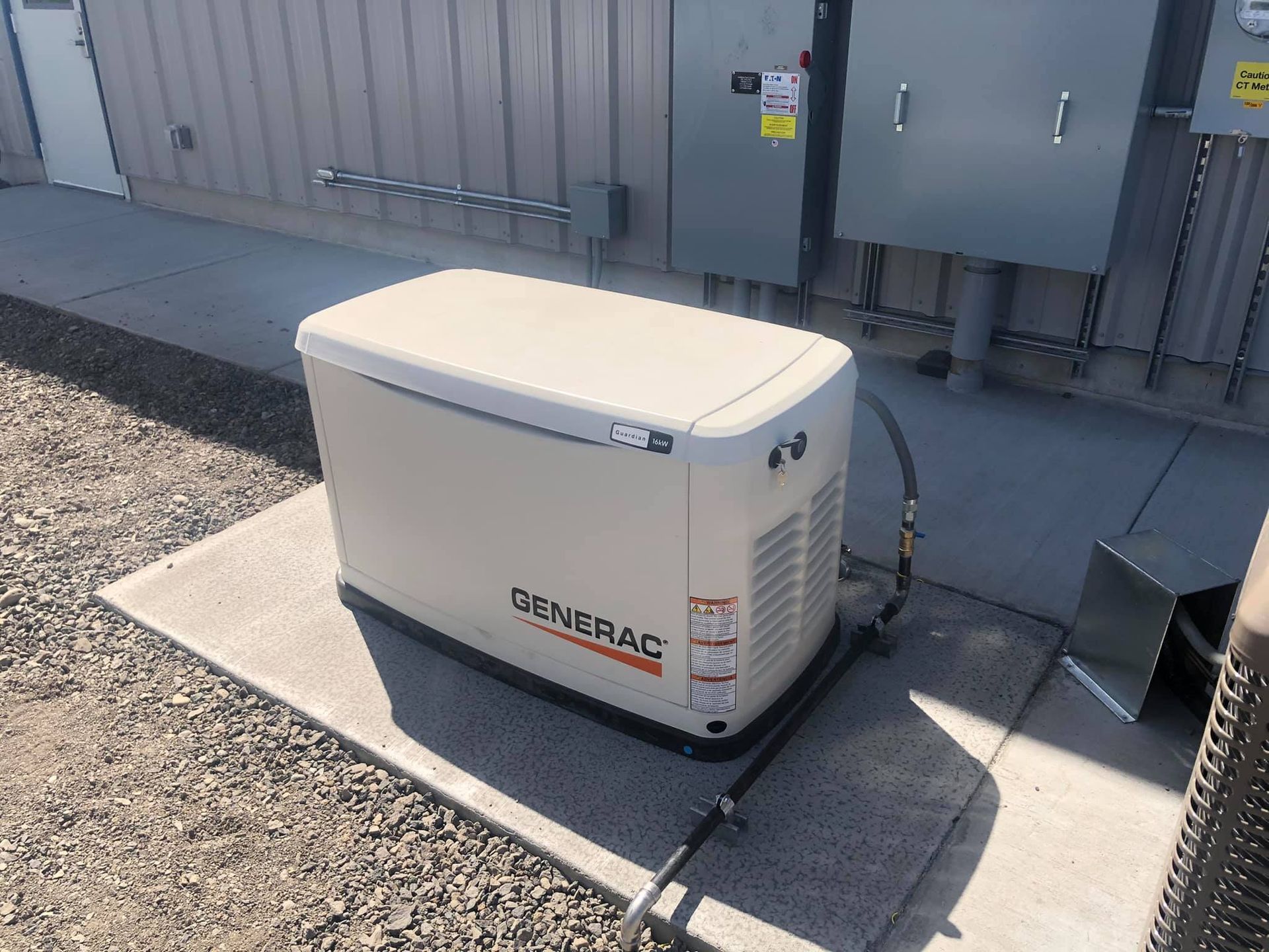 Generac generator, beige with black accents, on a concrete pad next to a building with electrical boxes.