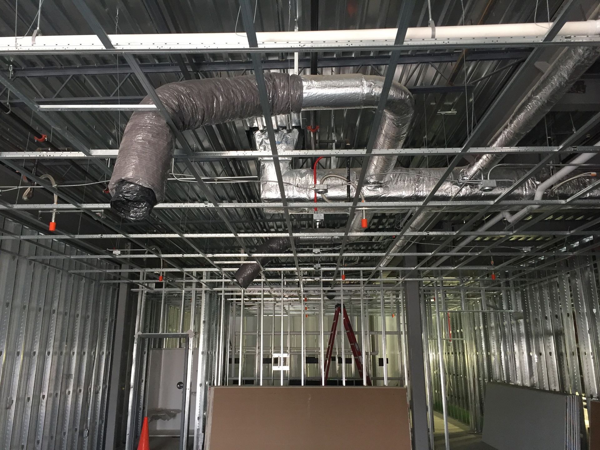 Interior view of a building under construction, showing metal framing, ductwork, and exposed ceiling.