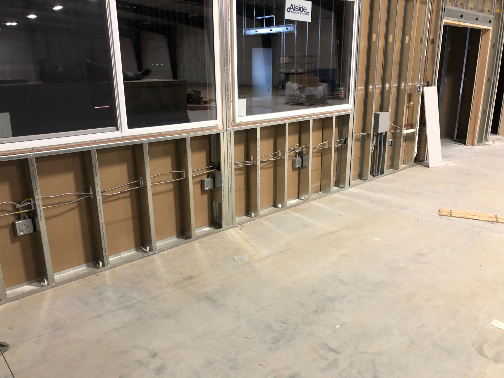 Interior view of a building under construction. Studs and wiring are visible behind windows, alongside electrical boxes.