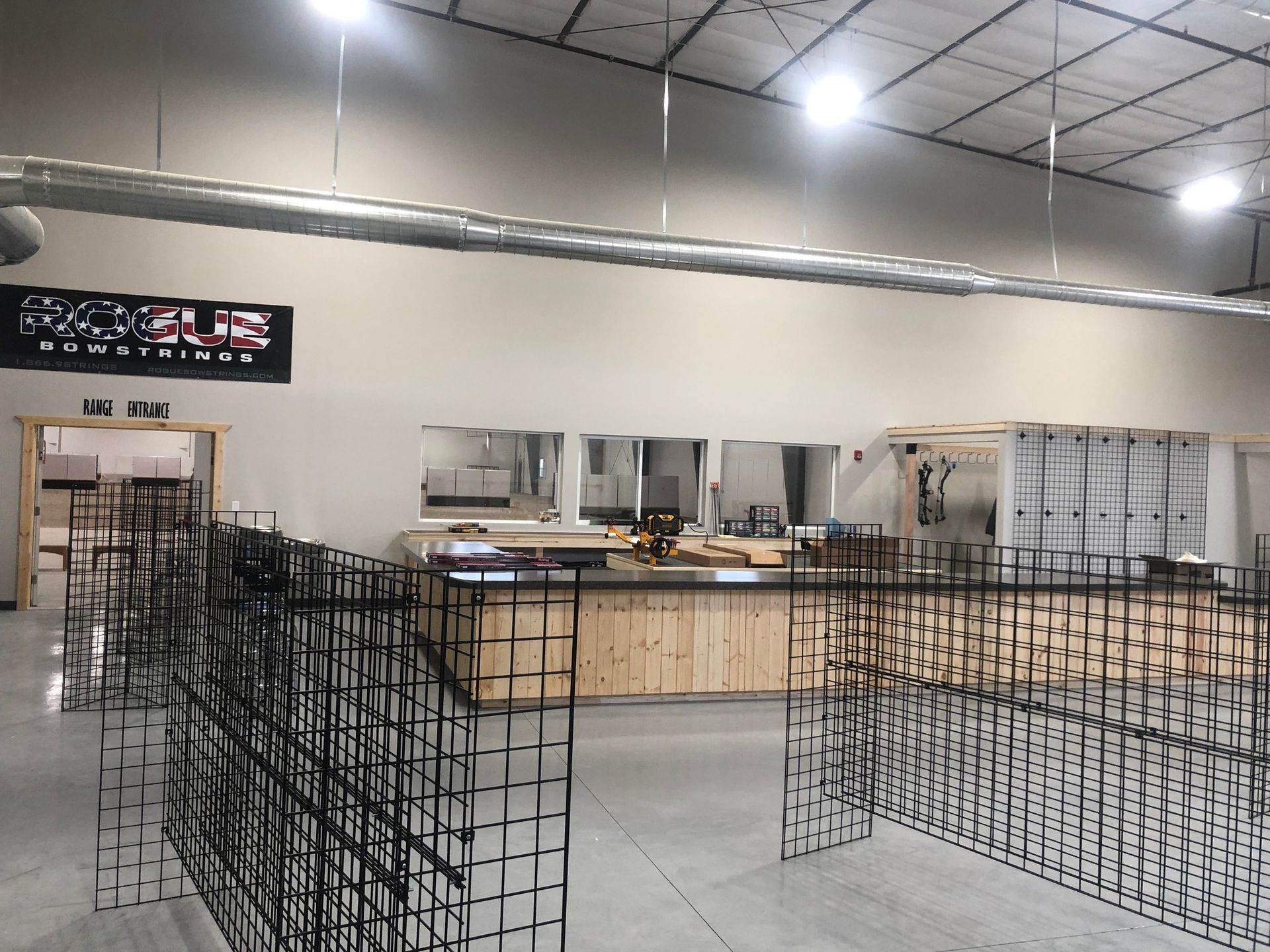 Empty warehouse interior with metal grid displays, wooden counters, and overhead ductwork.