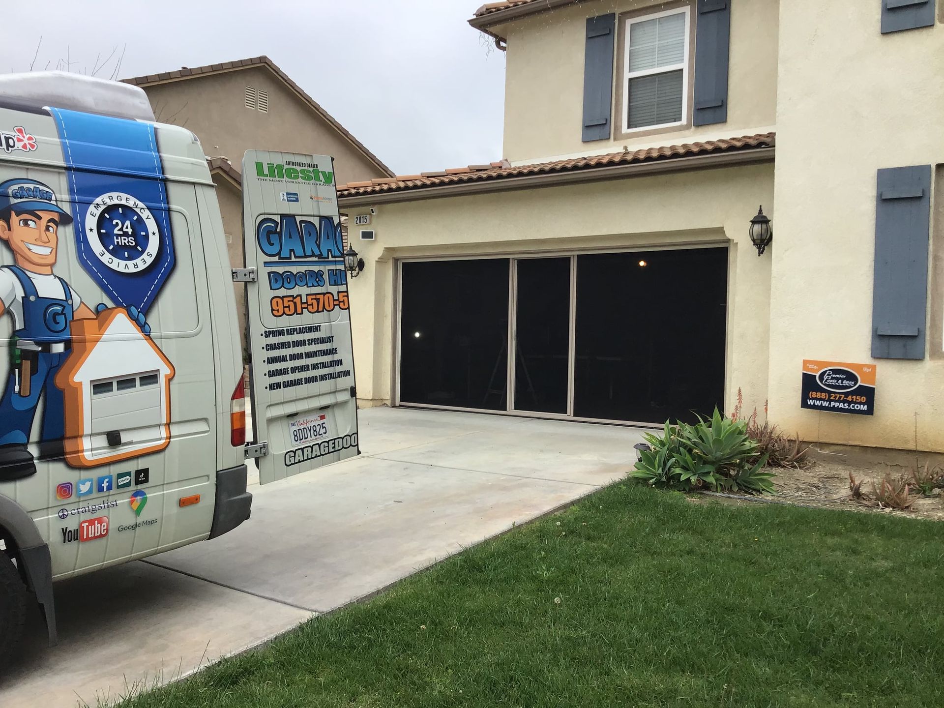 A van with a man on the back is parked in front of a house.