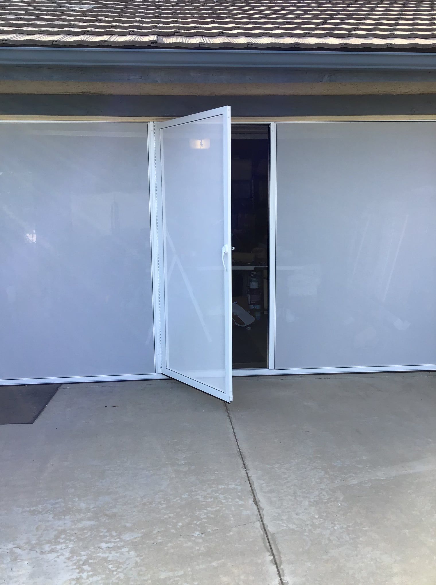A white screen door is open to a garage door.
