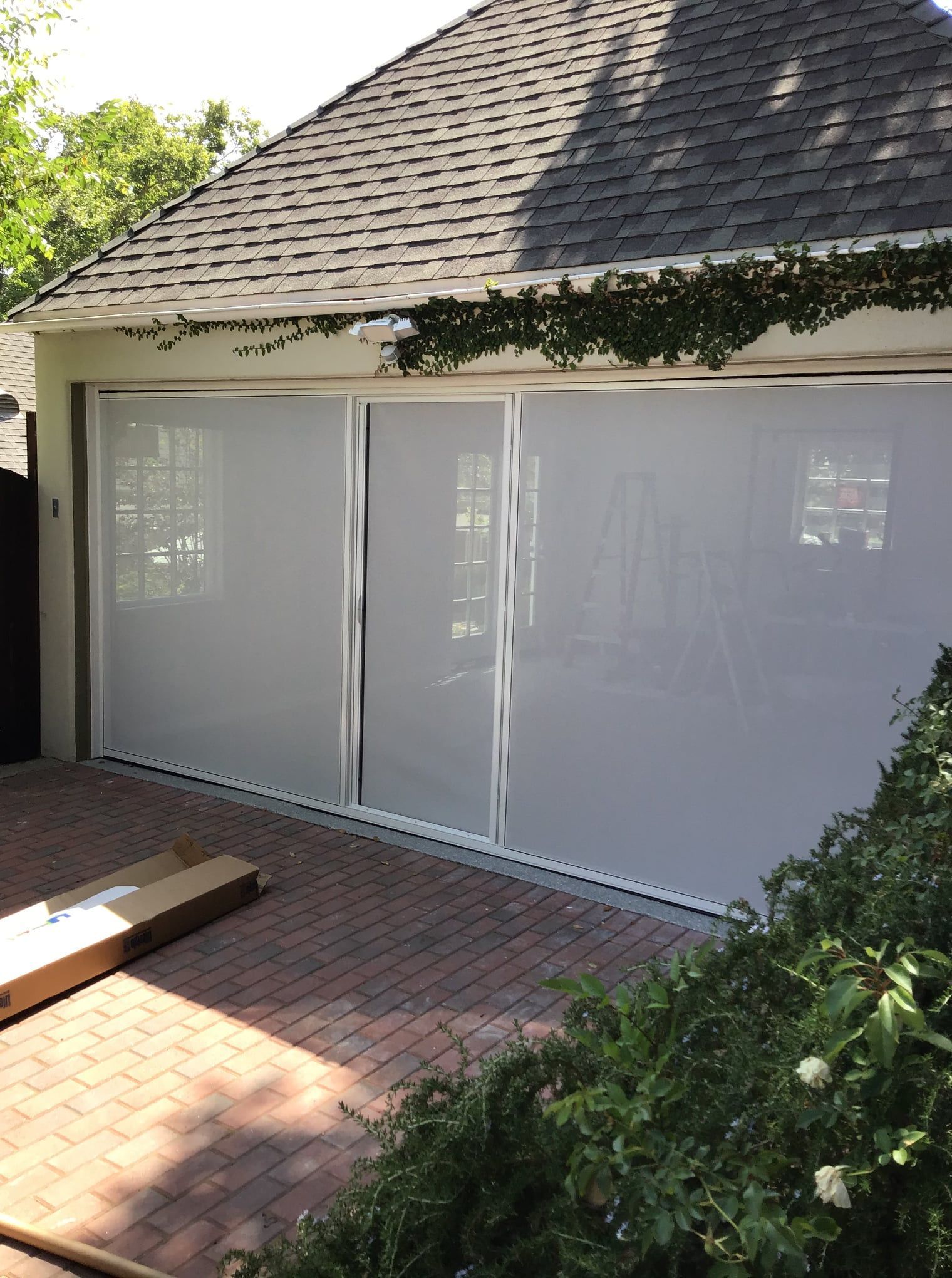 A garage door with white blinds on it and a brick driveway.