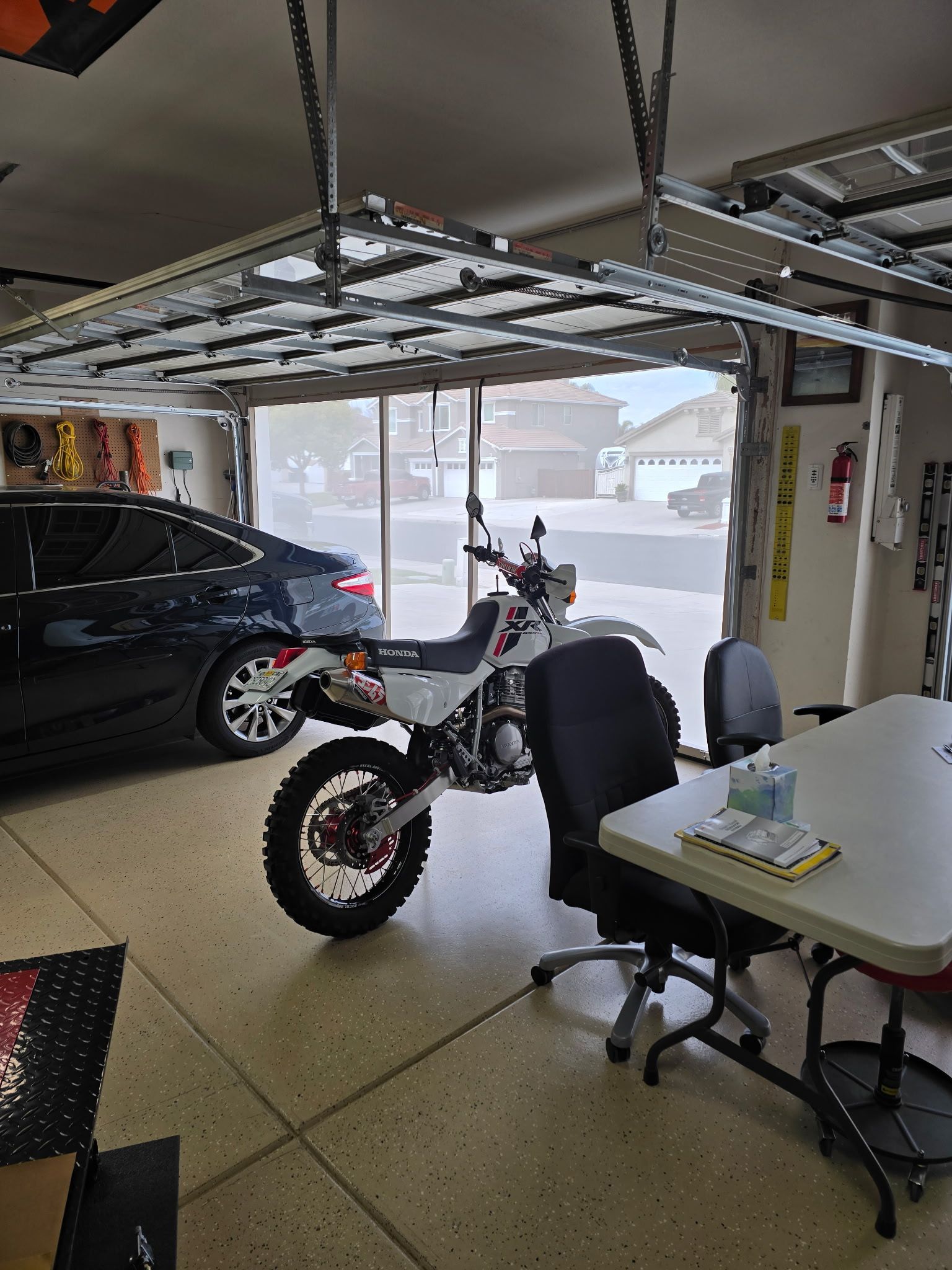 A motorcycle is parked in a garage next to a table and chairs.