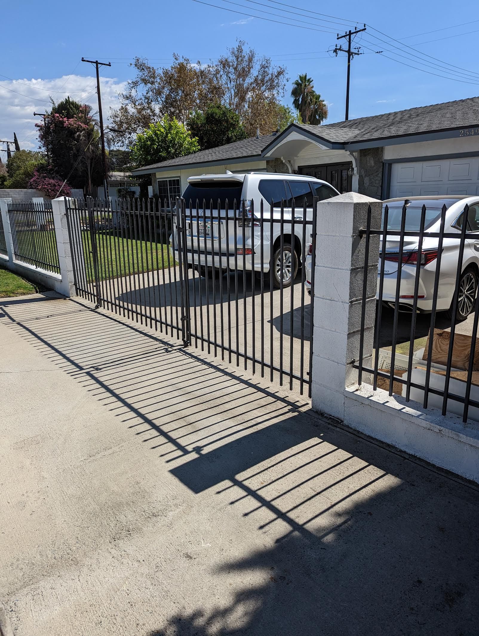 A white van is parked in front of a house behind a wrought iron fence.