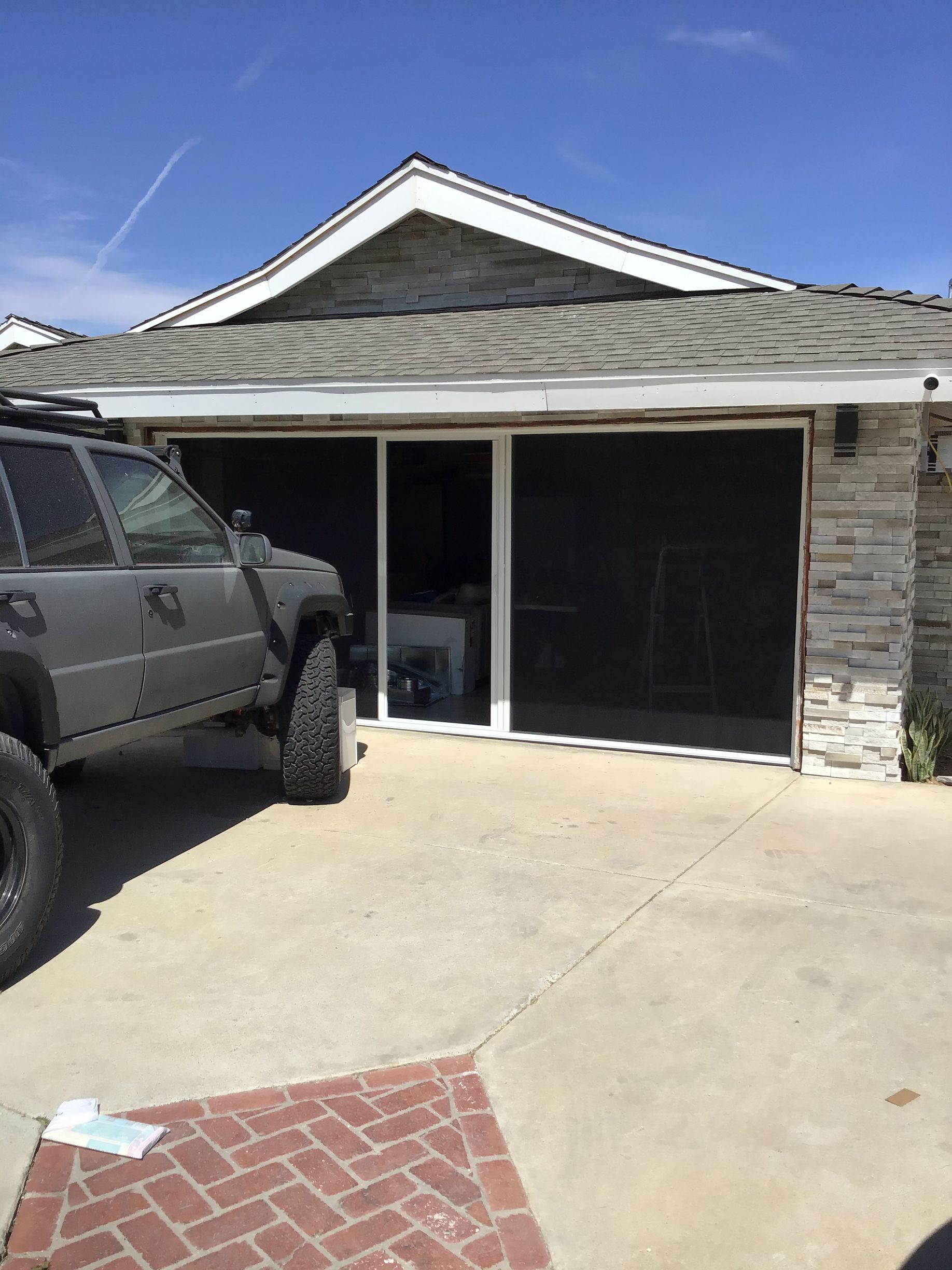 A car is parked in front of a house with screened in garage doors.