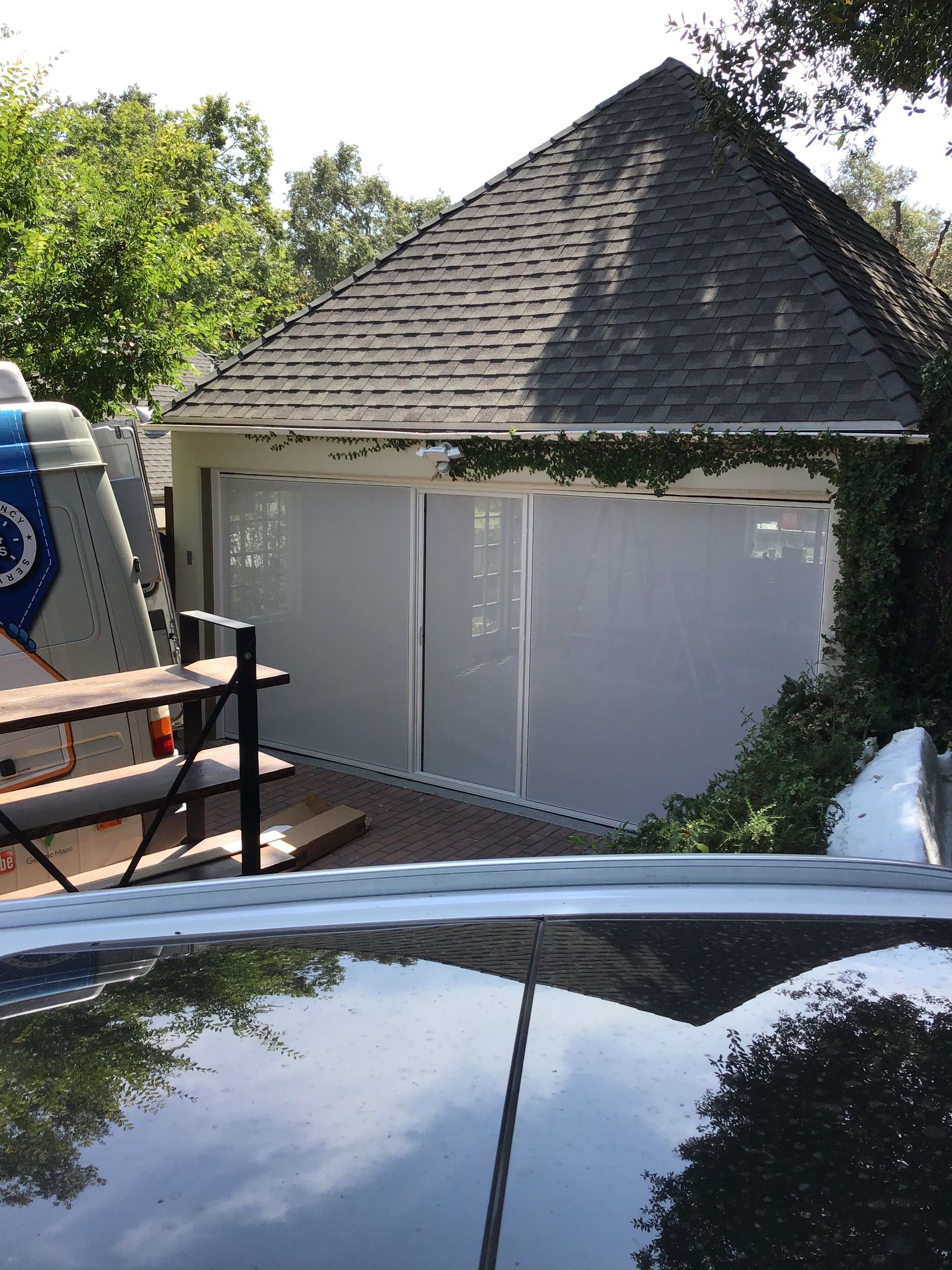 A car is parked in front of a house with a roof that is covered in shingles.