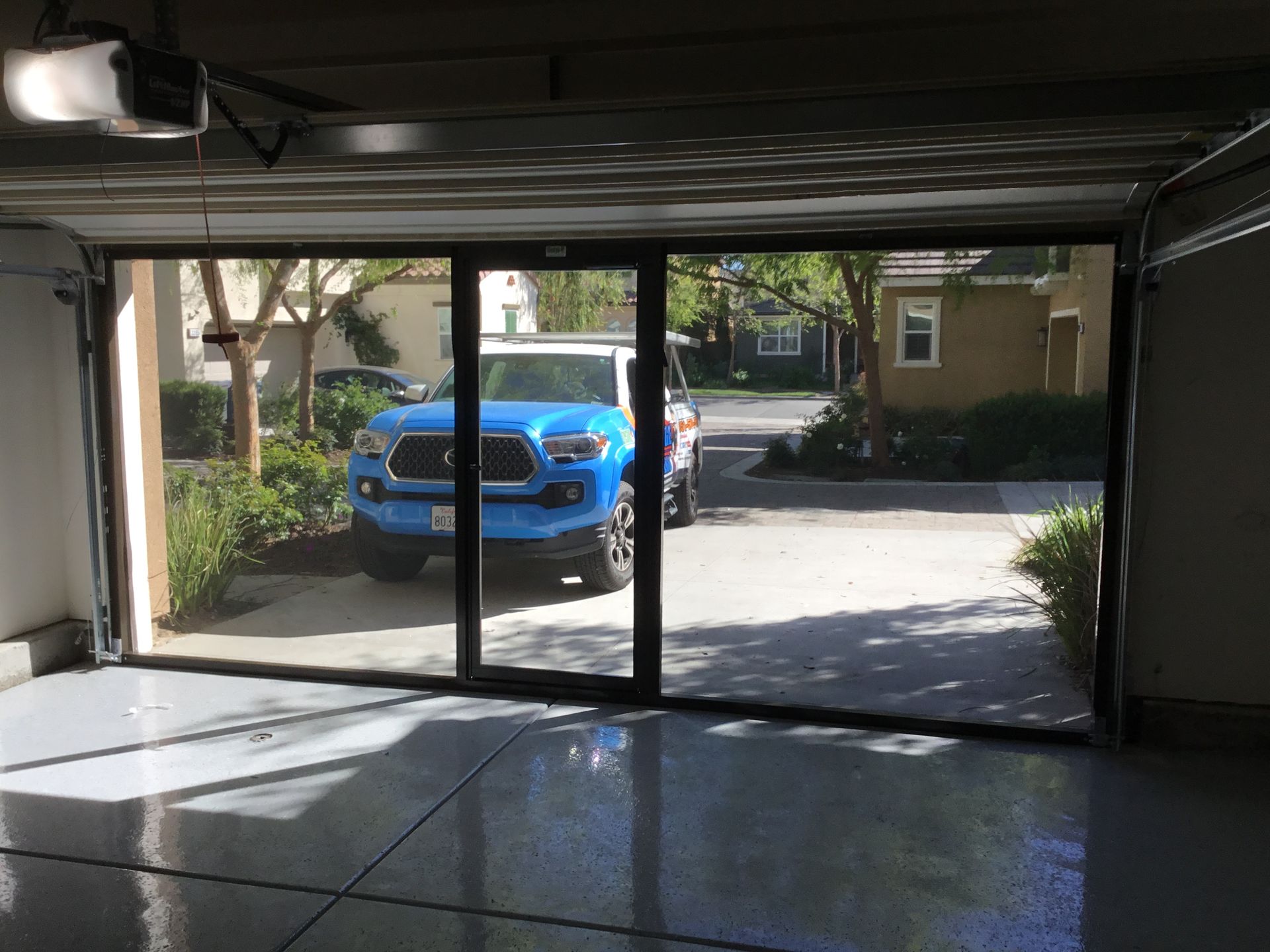 A blue truck is parked in a garage with a sliding glass door.
