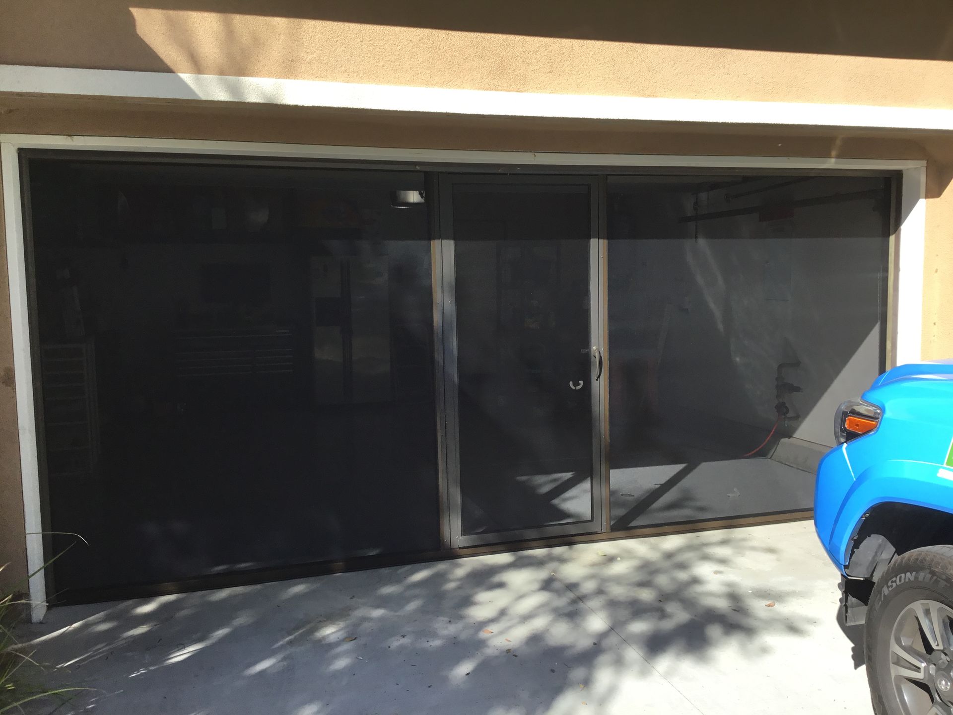 A blue truck is parked in front of a screened in garage door.