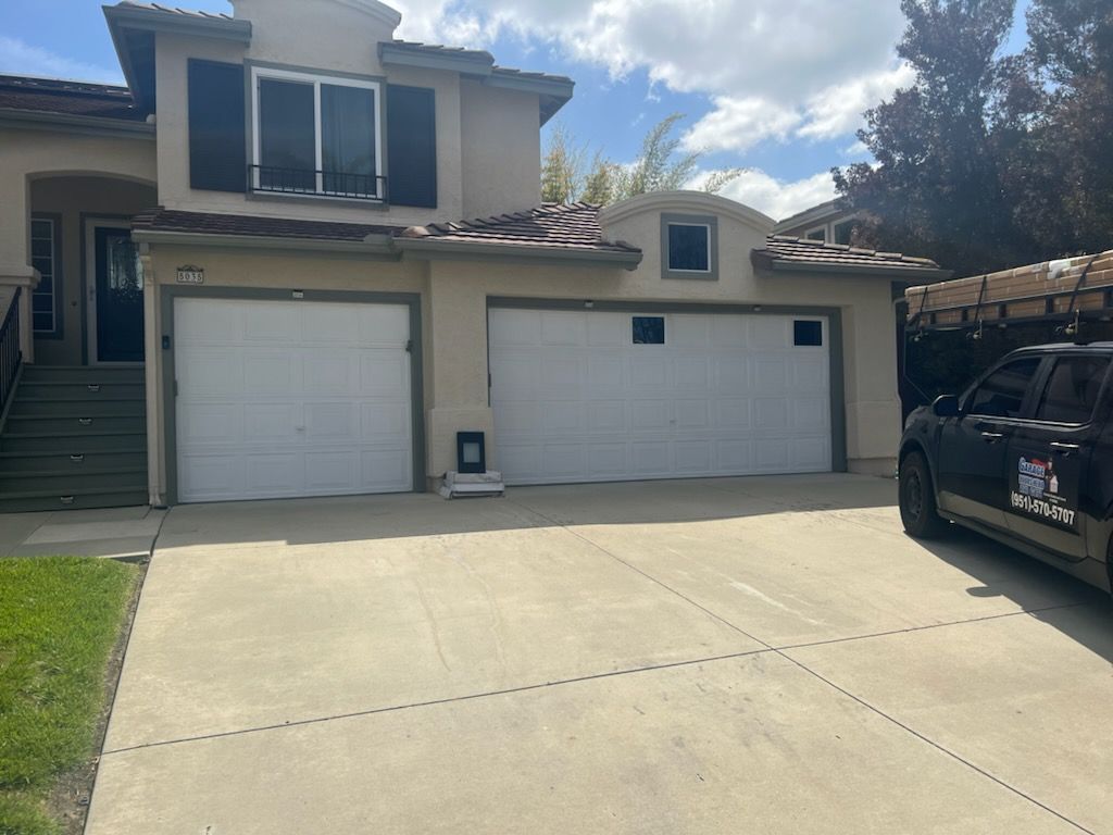 A car is parked in front of a house with two garage doors.