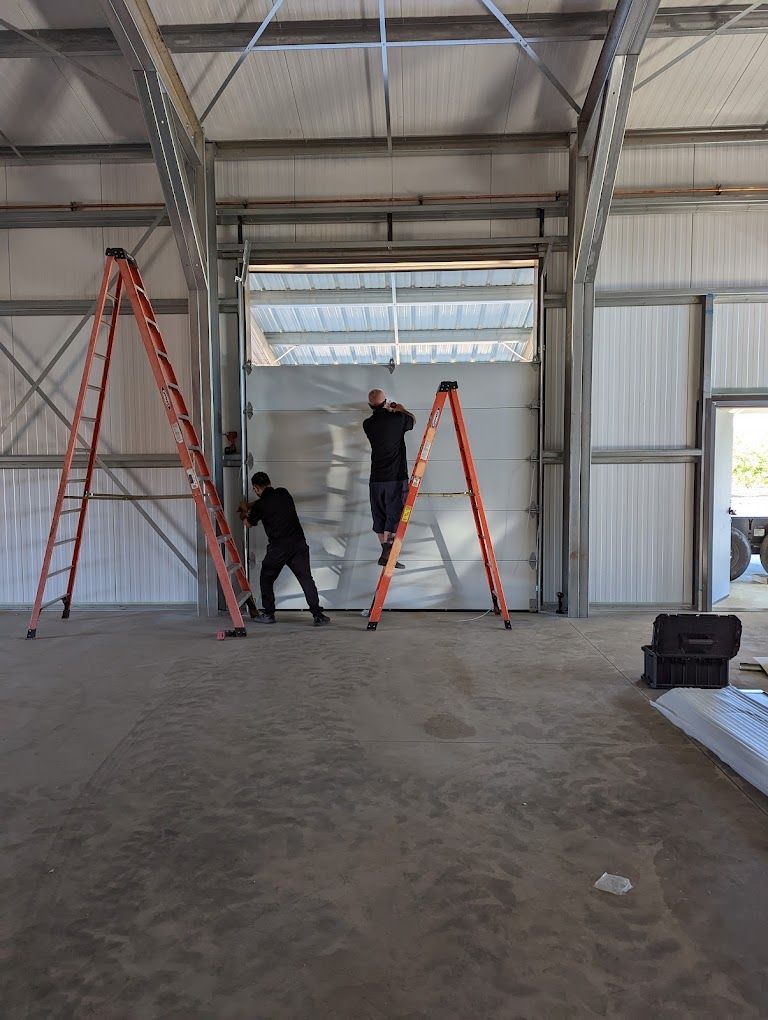 Two men are working on a garage door with ladders.