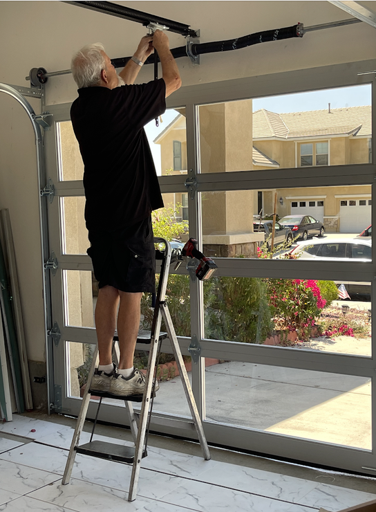 A man is standing on a ladder fixing a garage door.