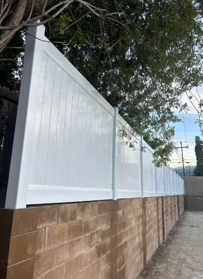 A white fence is sitting on top of a brick wall.