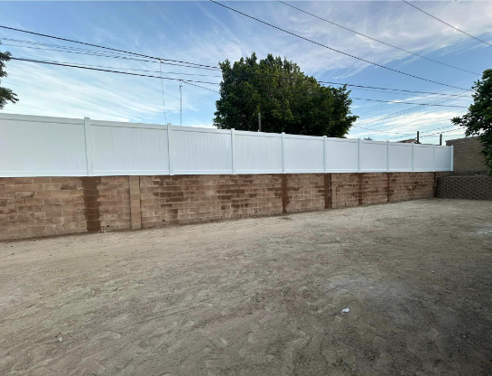 A large white fence is surrounding a brick wall.