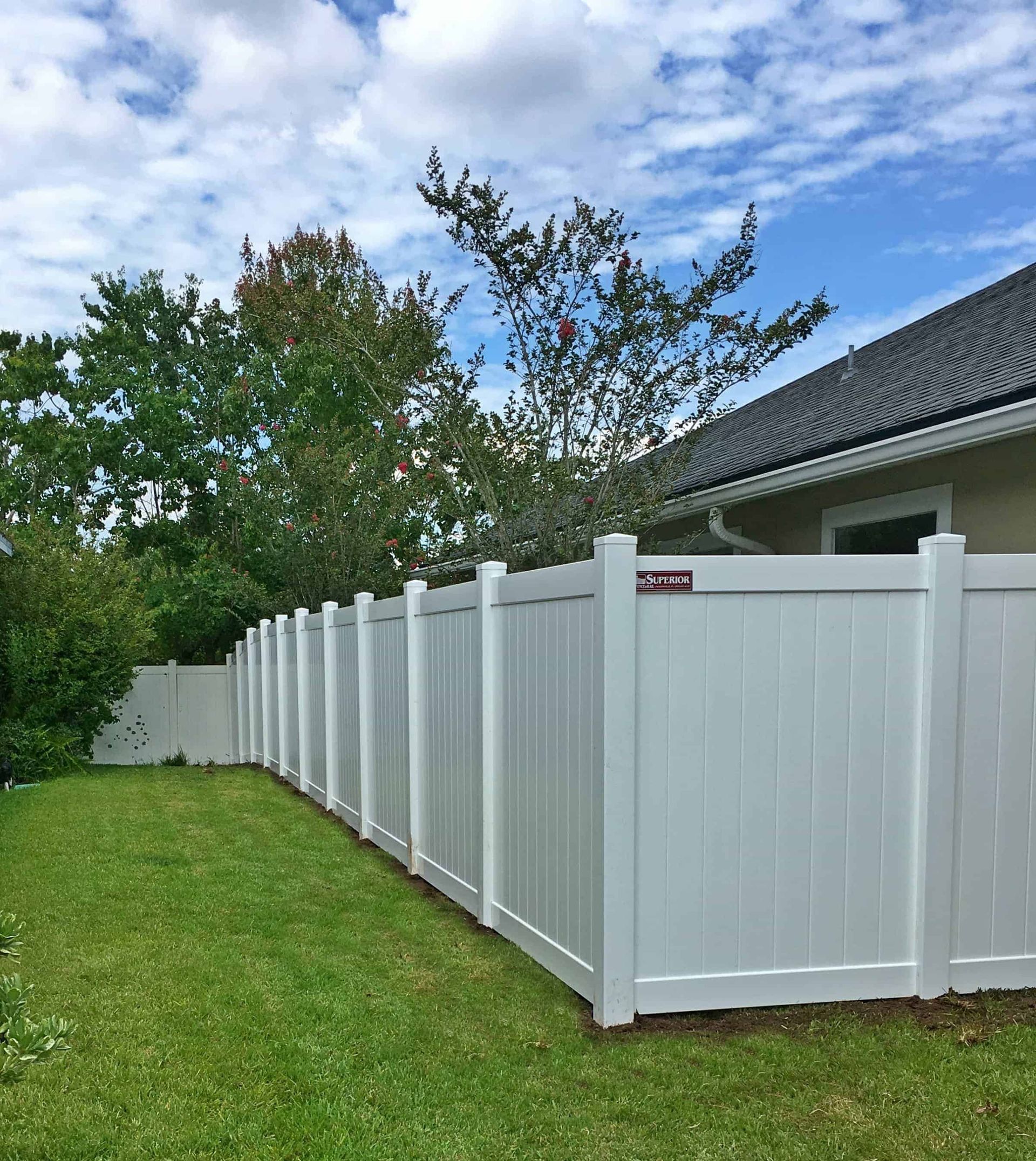 A white vinyl fence surrounds a lush green yard in front of a house.