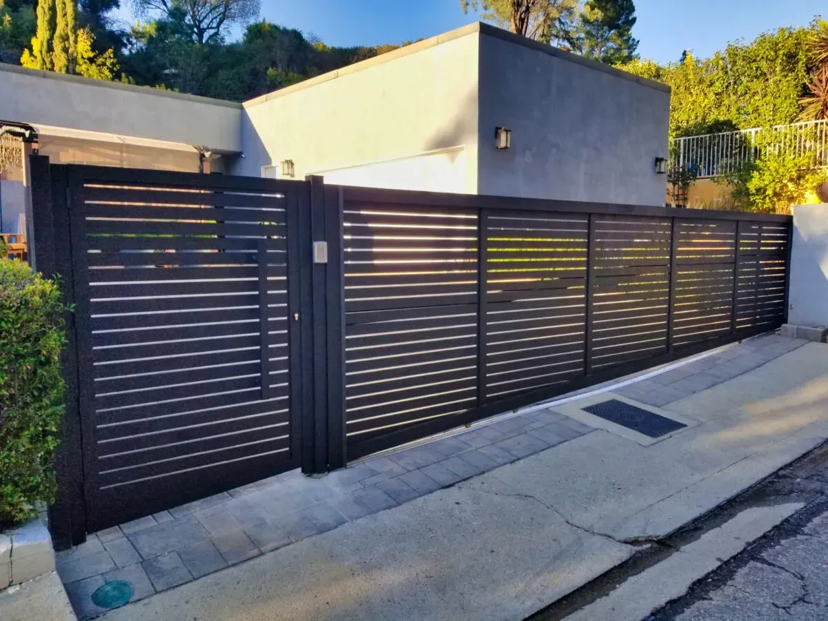 A sliding gate is sitting on the side of a road in front of a house.