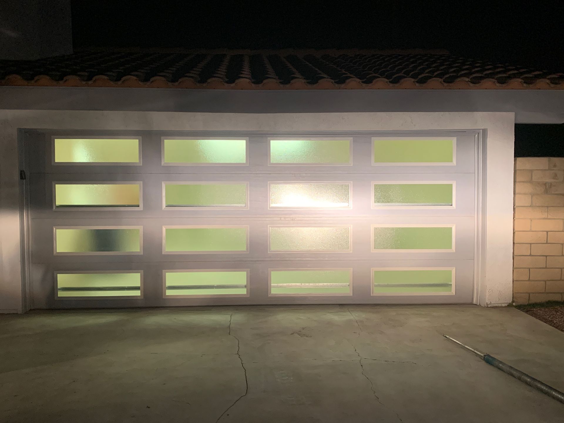 A white garage door with a lot of windows is lit up at night.