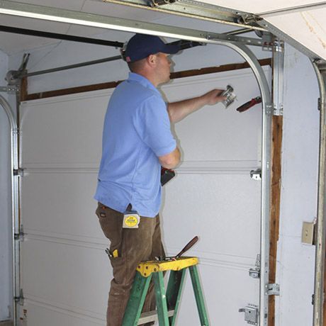 A man is standing on a ladder fixing a garage door.