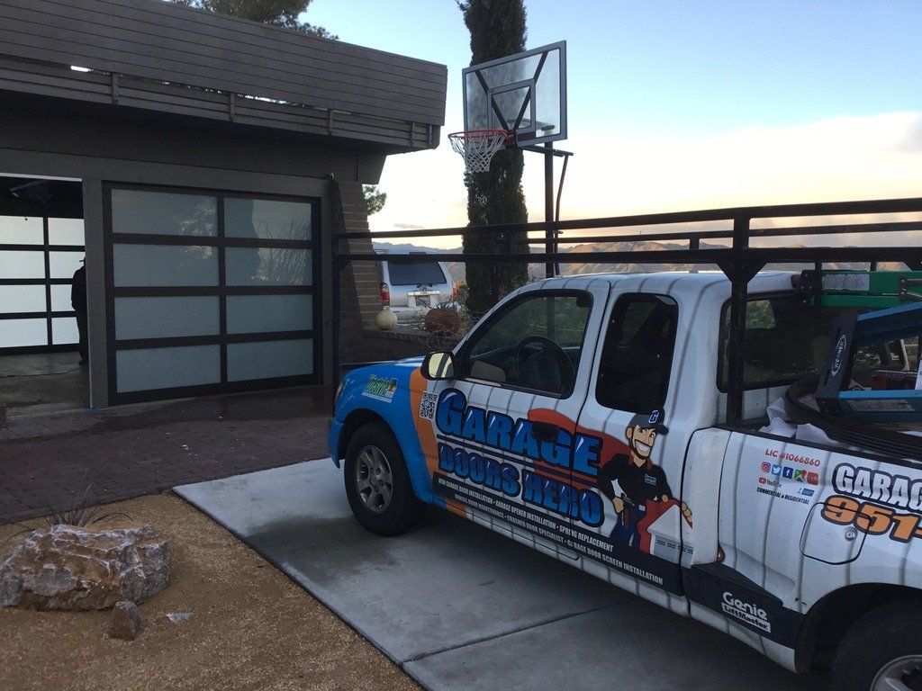 A white truck is parked in front of a garage door with a basketball hoop in the background.