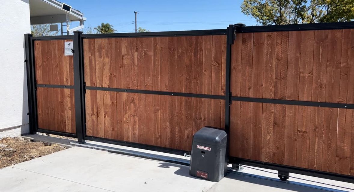 A wooden gate with a motor attached to it is sitting next to a concrete driveway.