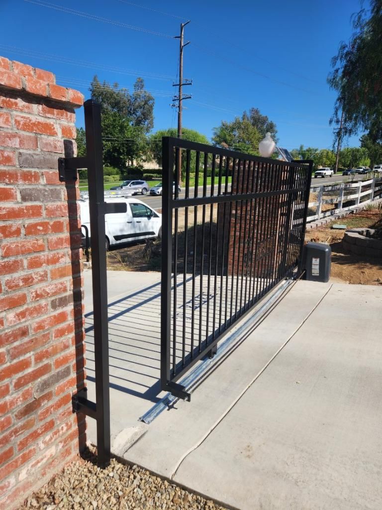 A black gate is open to a driveway next to a brick wall.