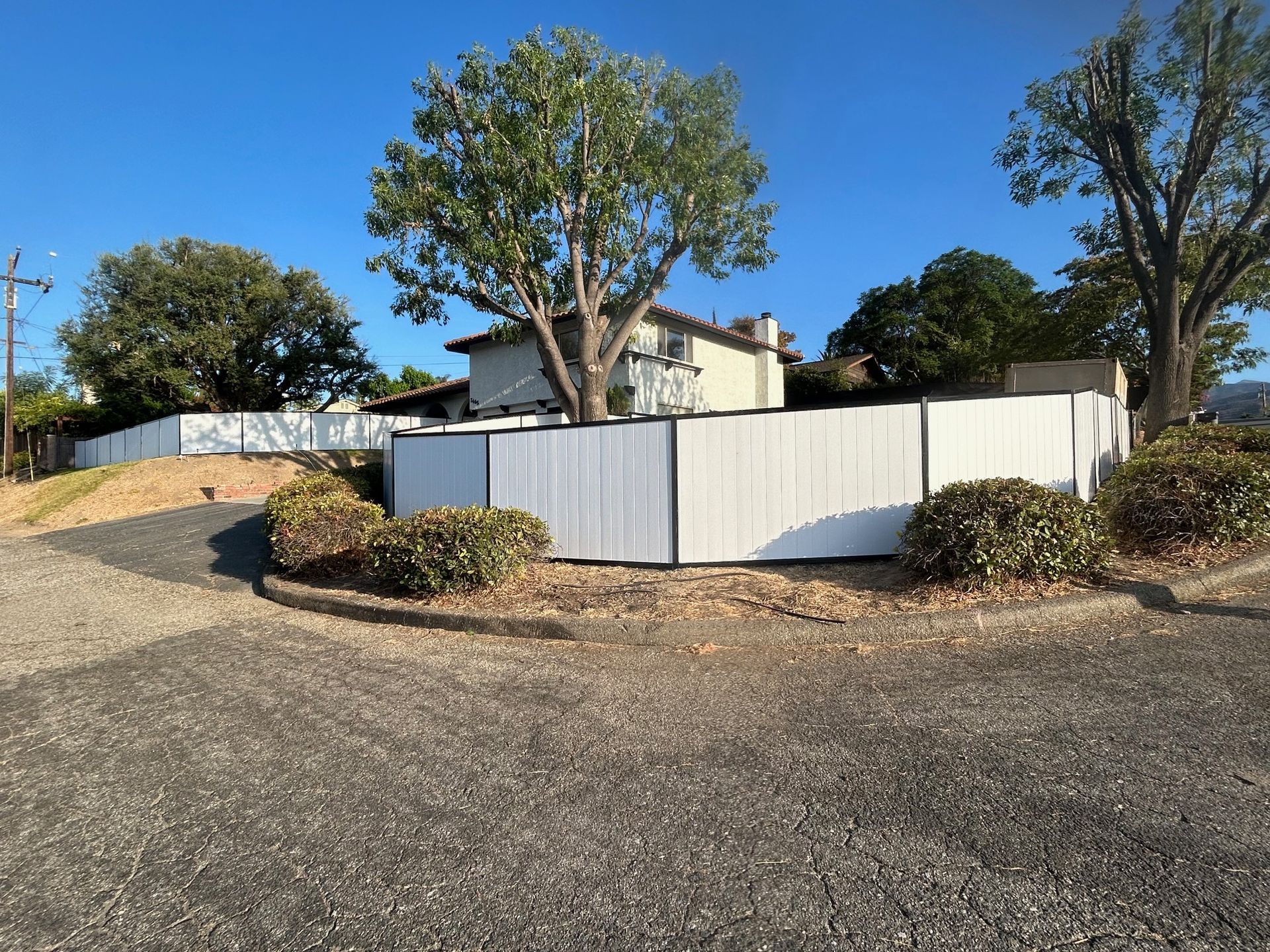 A white fence is surrounded by bushes and trees in front of a house
