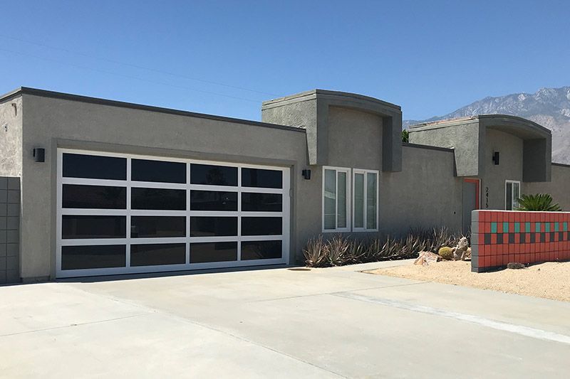 A modern house with a large garage door and mountains in the background.