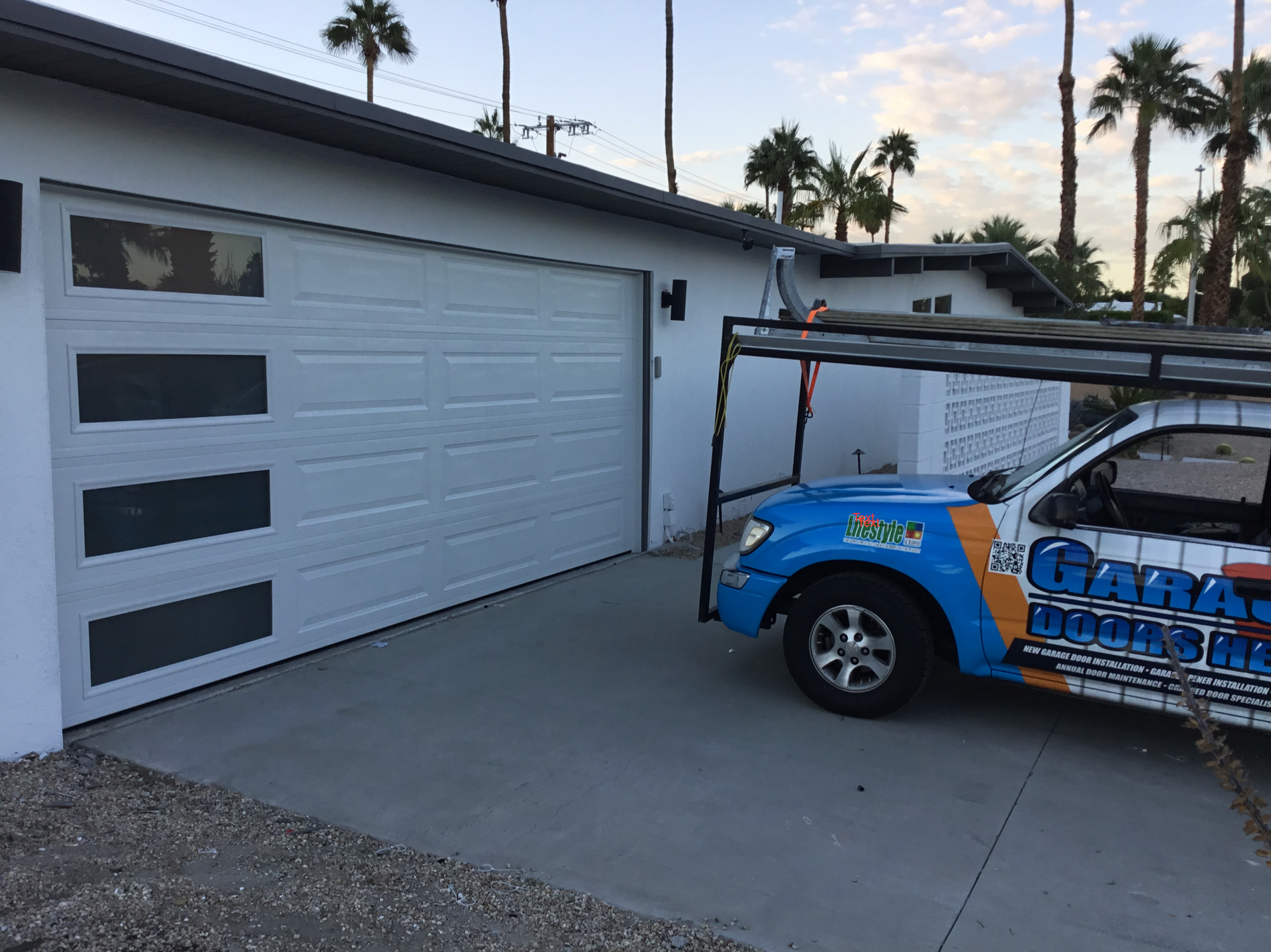 A blue garage door company truck is parked in front of a garage door.