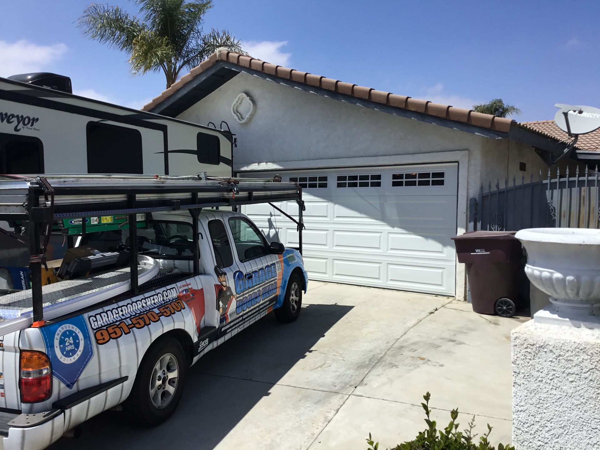 A truck is parked in front of a house with a trailer in the background.