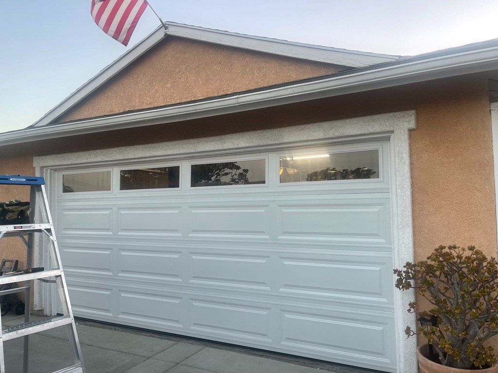 A white garage door is sitting on the side of a house next to a ladder.