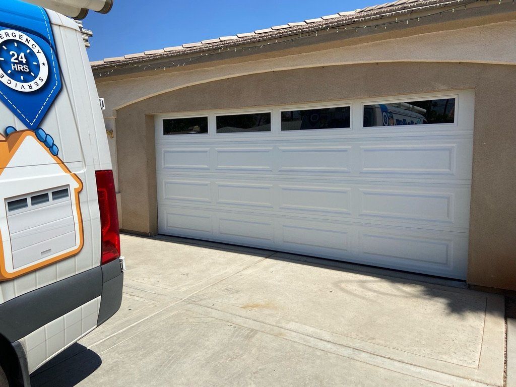A white van is parked in front of a white garage door.