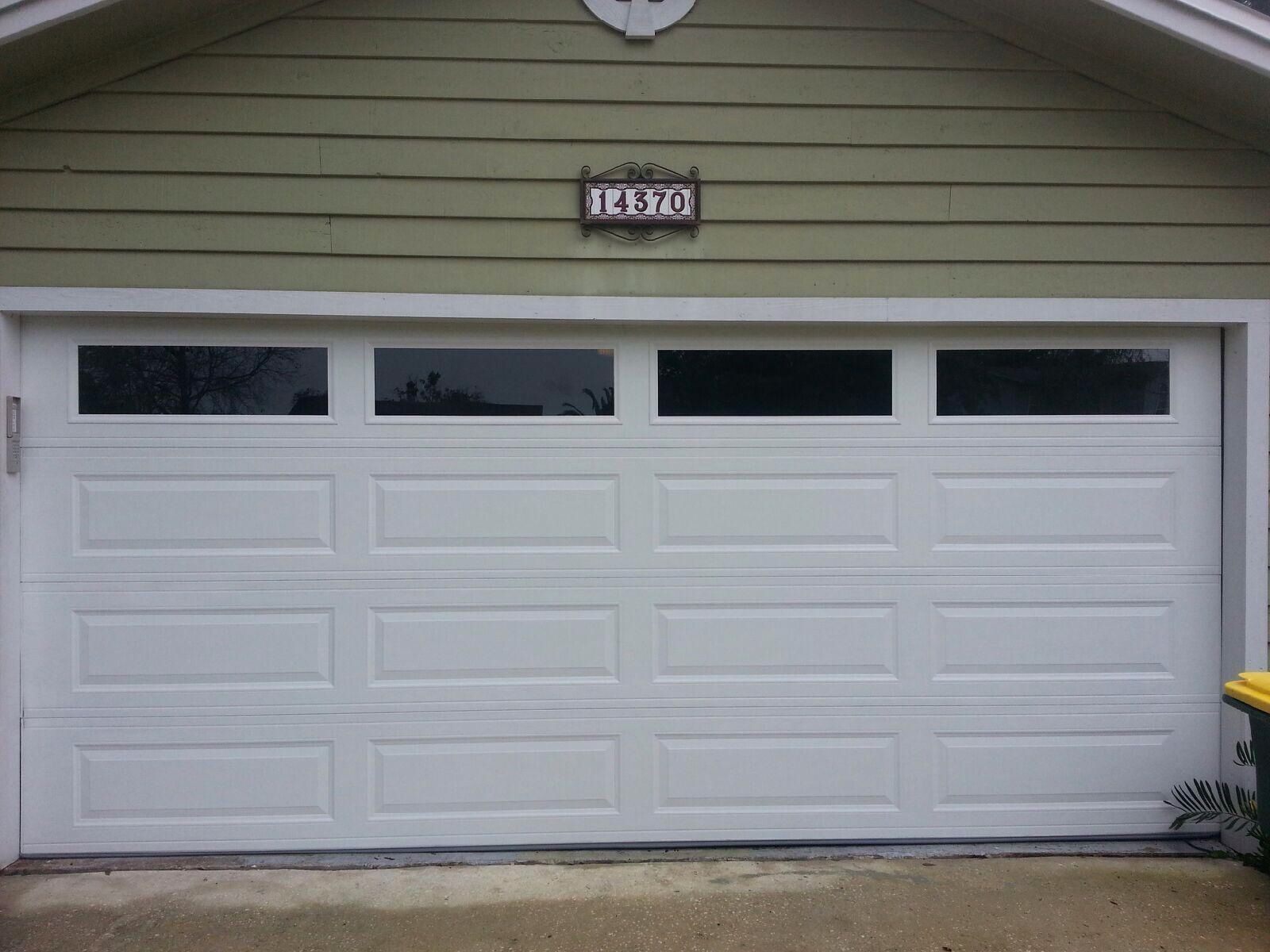 A white garage door is sitting in front of a green house.